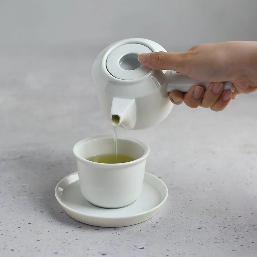 Tee wie aus einer weißen Teekanne in eine Tasse geschüttet